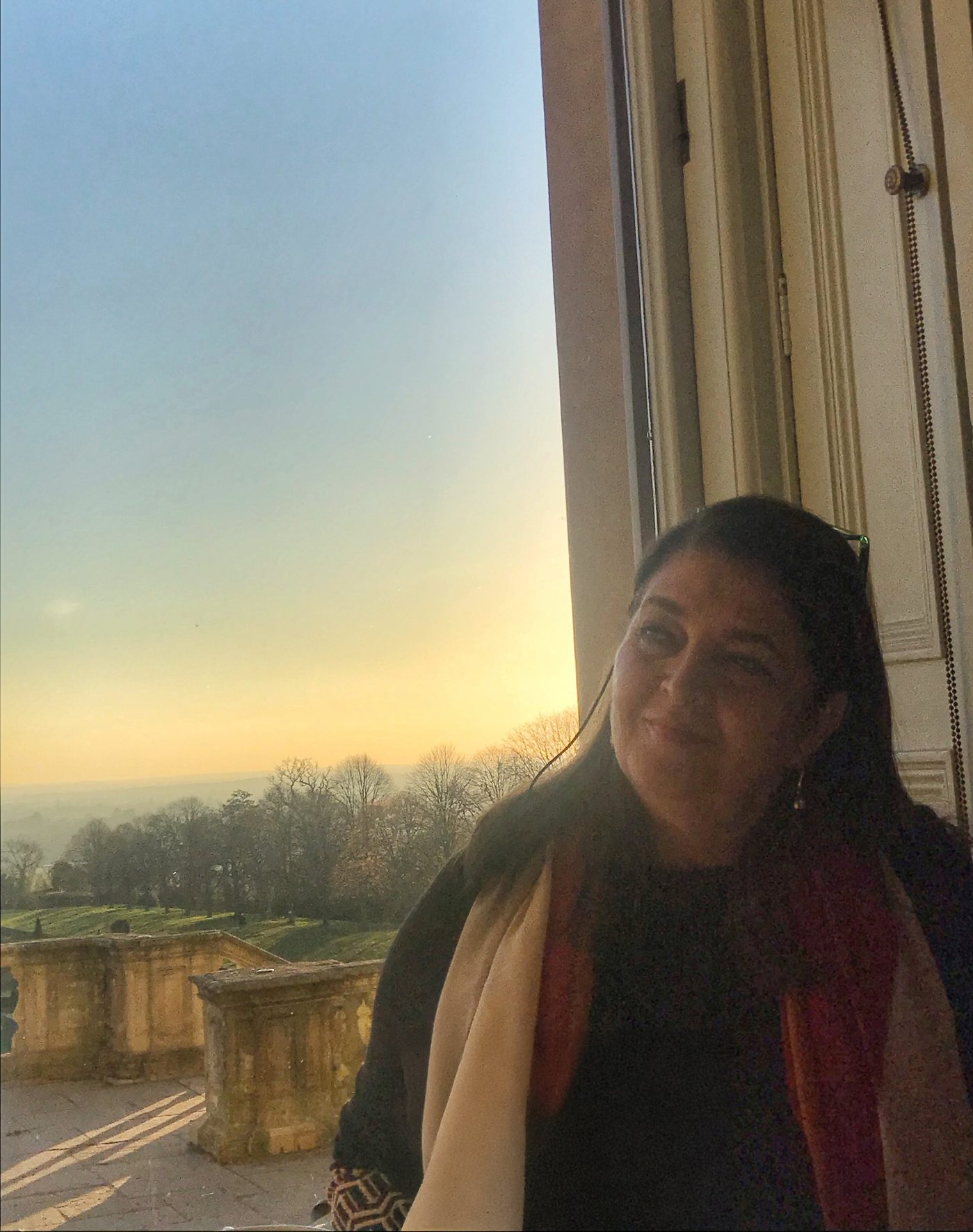 Hana Karam at a window, looking out over a valley at sunset.